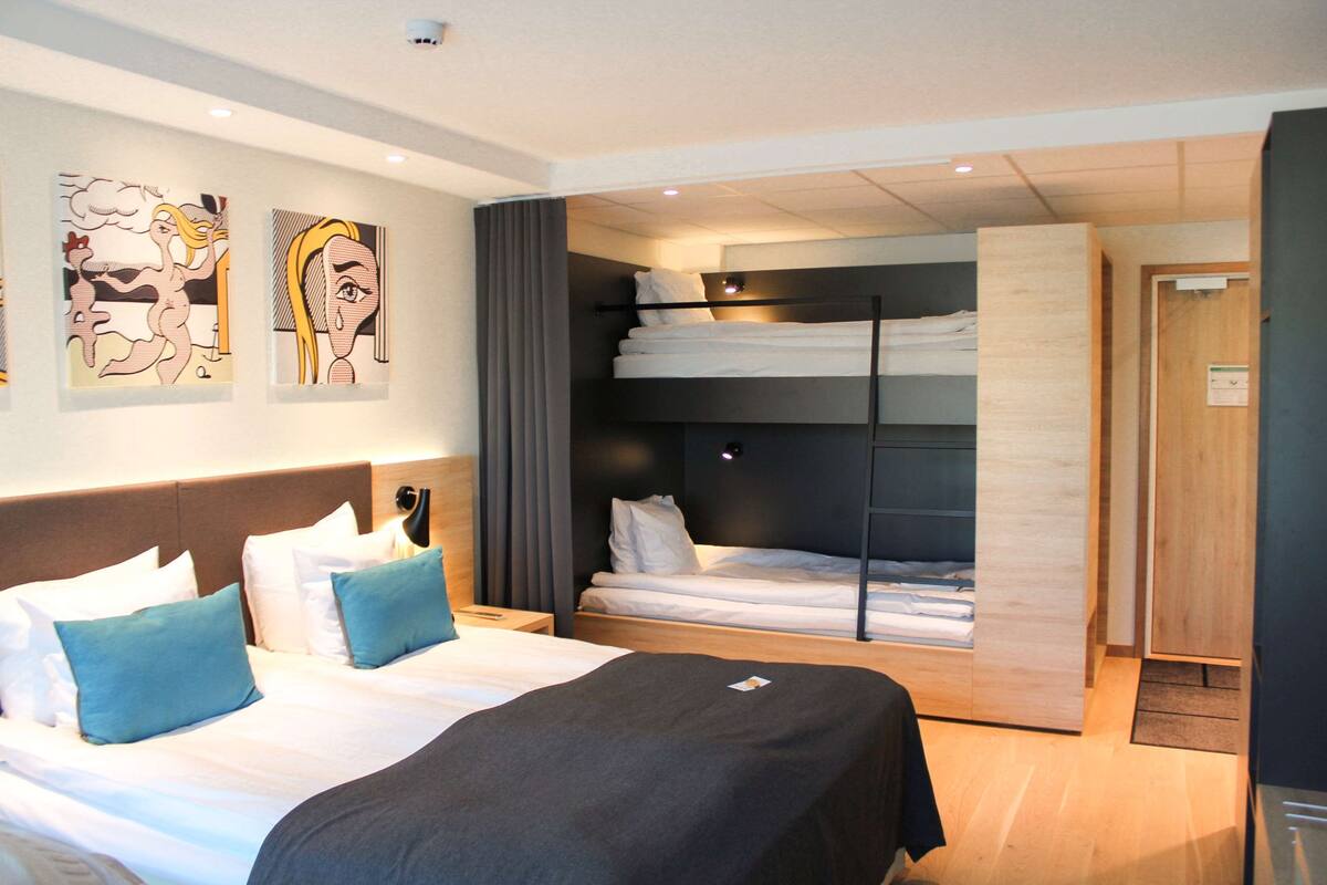 A hotel room with two beds, a large artwork on the wall, and a wooden door.