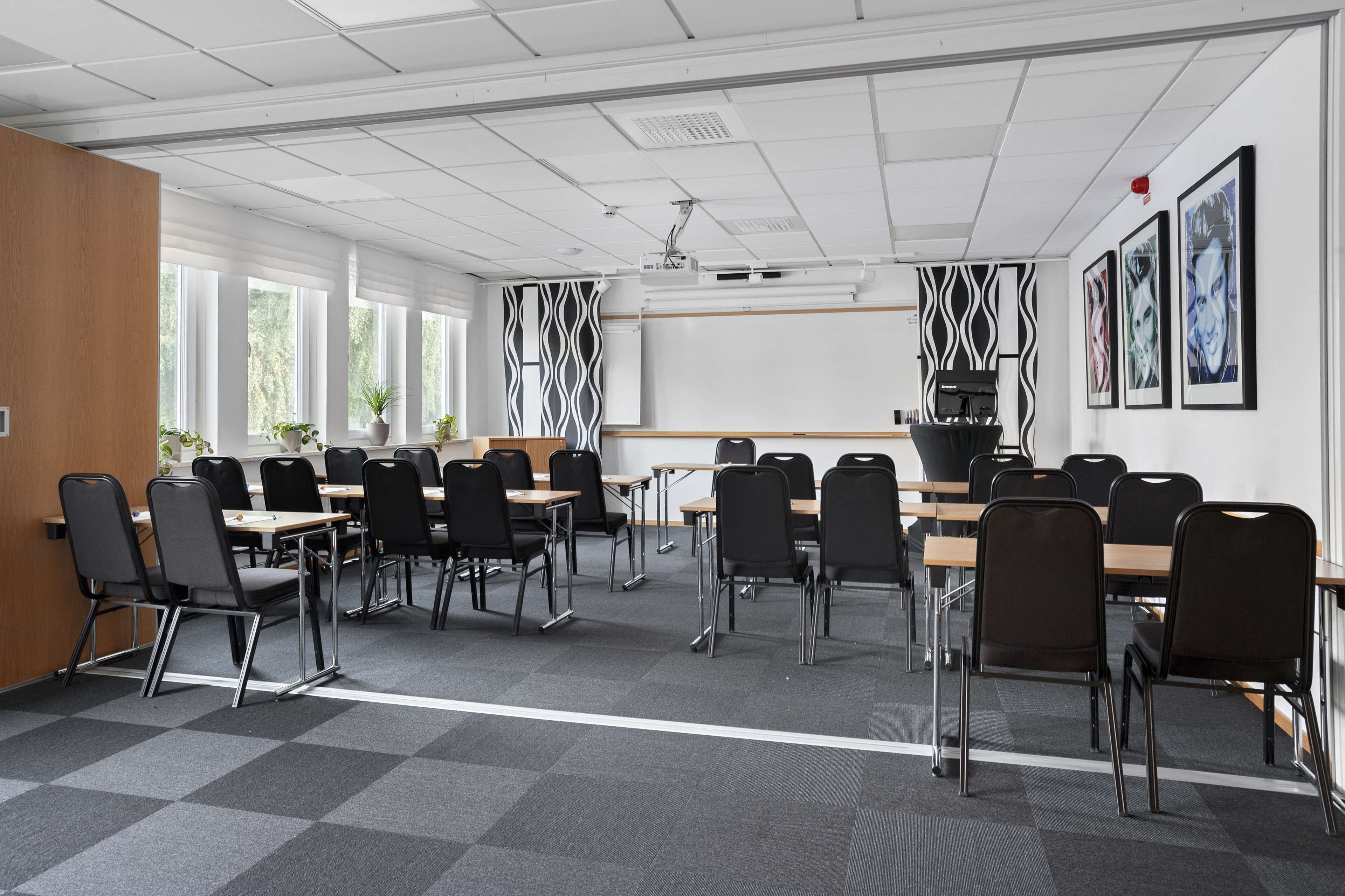 A conference room with multiple tables and chairs, large windows, and wall-mounted artwork.