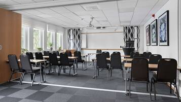 A conference room with multiple tables and chairs, large windows, and wall-mounted artwork.