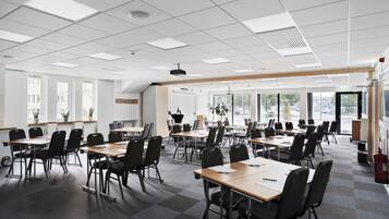 Un salón de conferencias con varias mesas y sillas, ventanas amplias e iluminación empotrada en el techo.