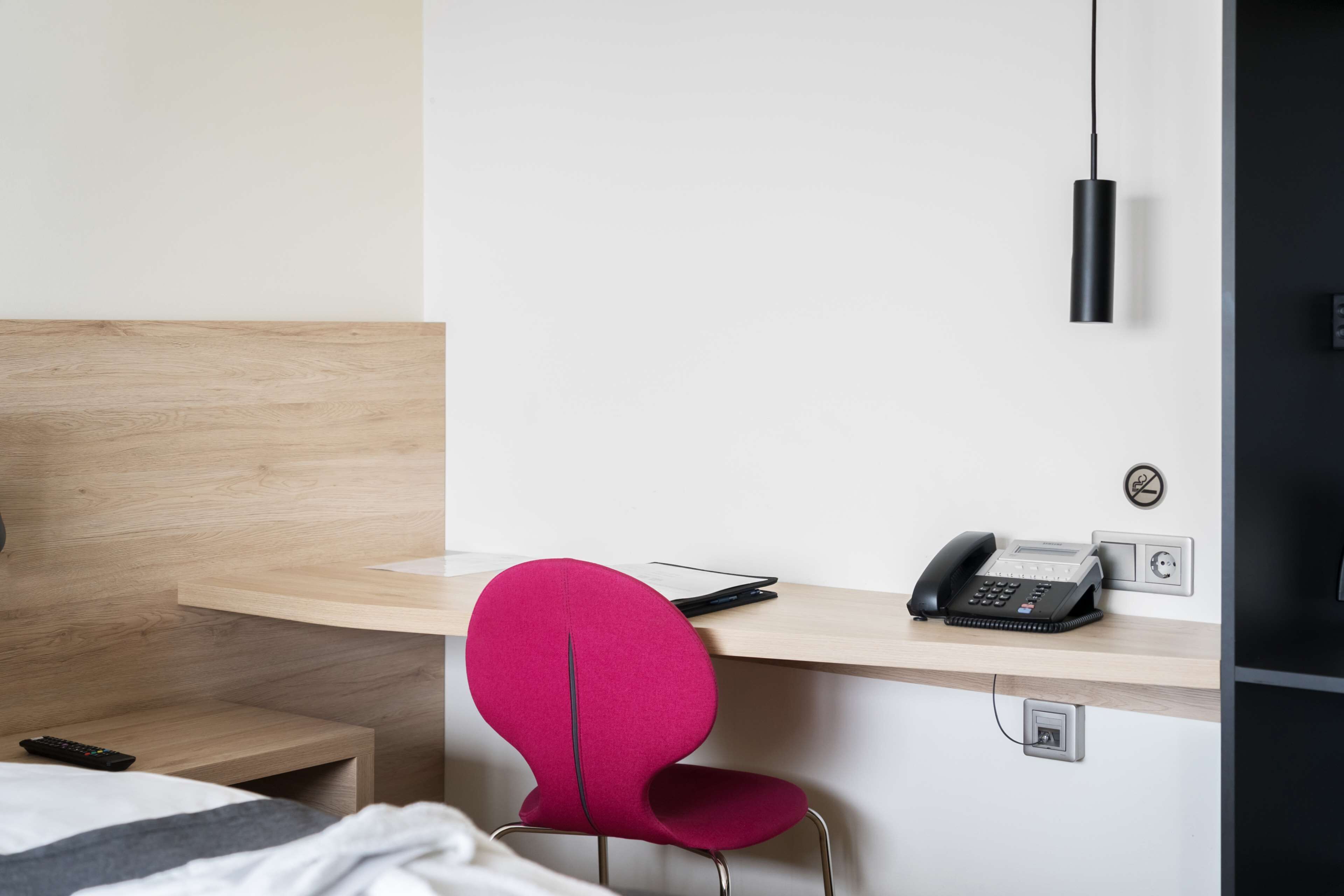 Habitació d'hotel amb escriptori de fusta, una cadira vermella, un telèfon negre i un llum d'ambient fixada a la paret.