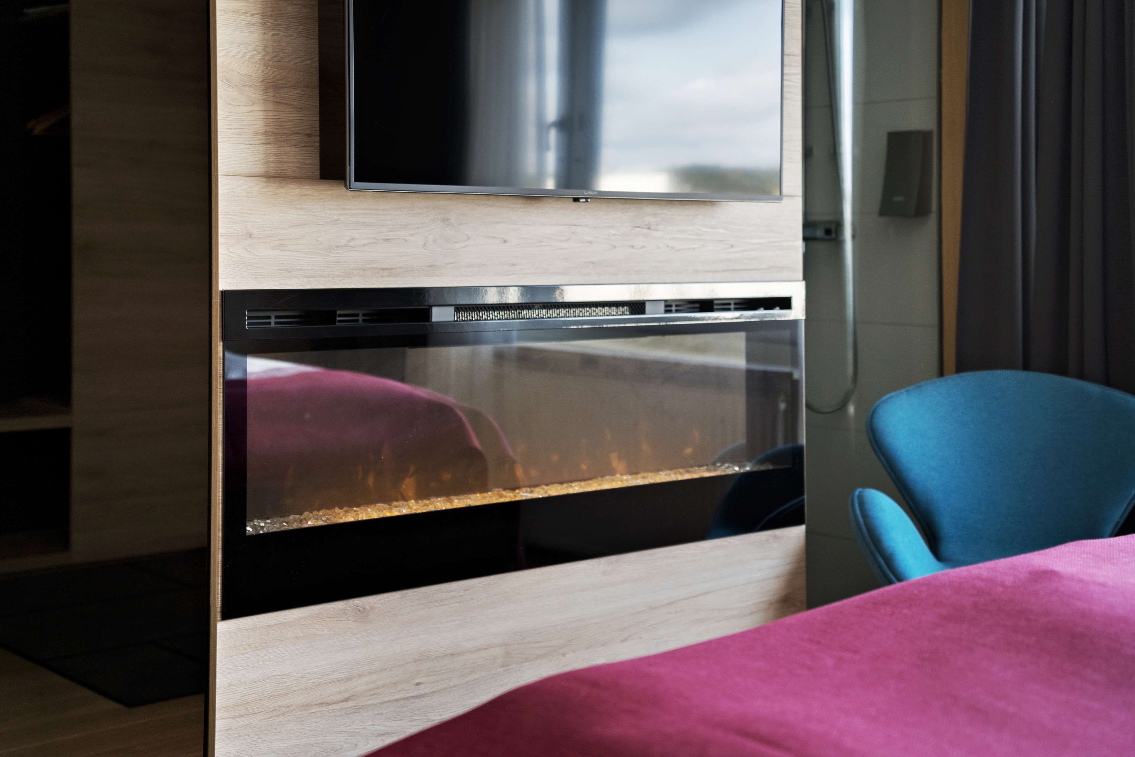 Una habitación moderna con horno integrado, un televisor de pantalla plana montado encima y una silla azul.