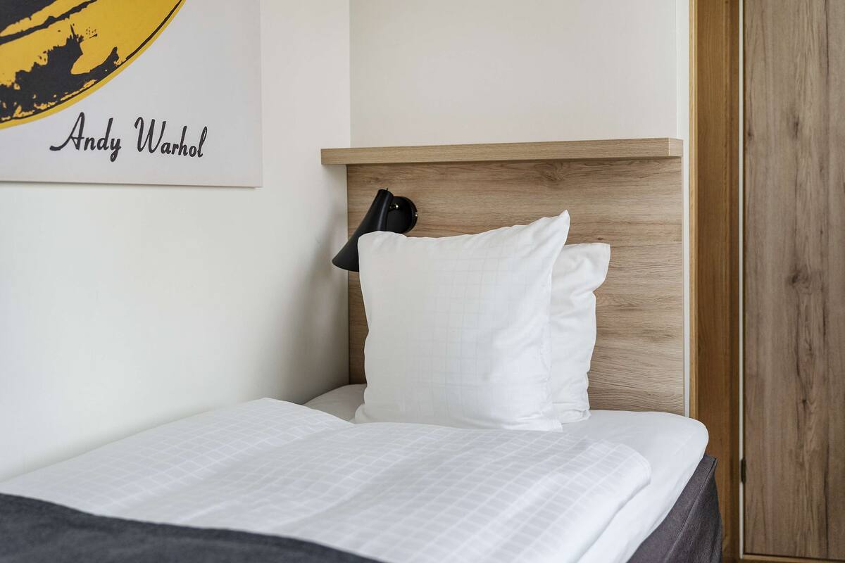 A neatly made bed with white bedding and a headboard, a black lamp, and a framed picture on the wall.