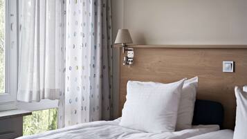 A hotel room with a bed, a window with curtains, a wall-mounted lamp, and a wooden headboard.