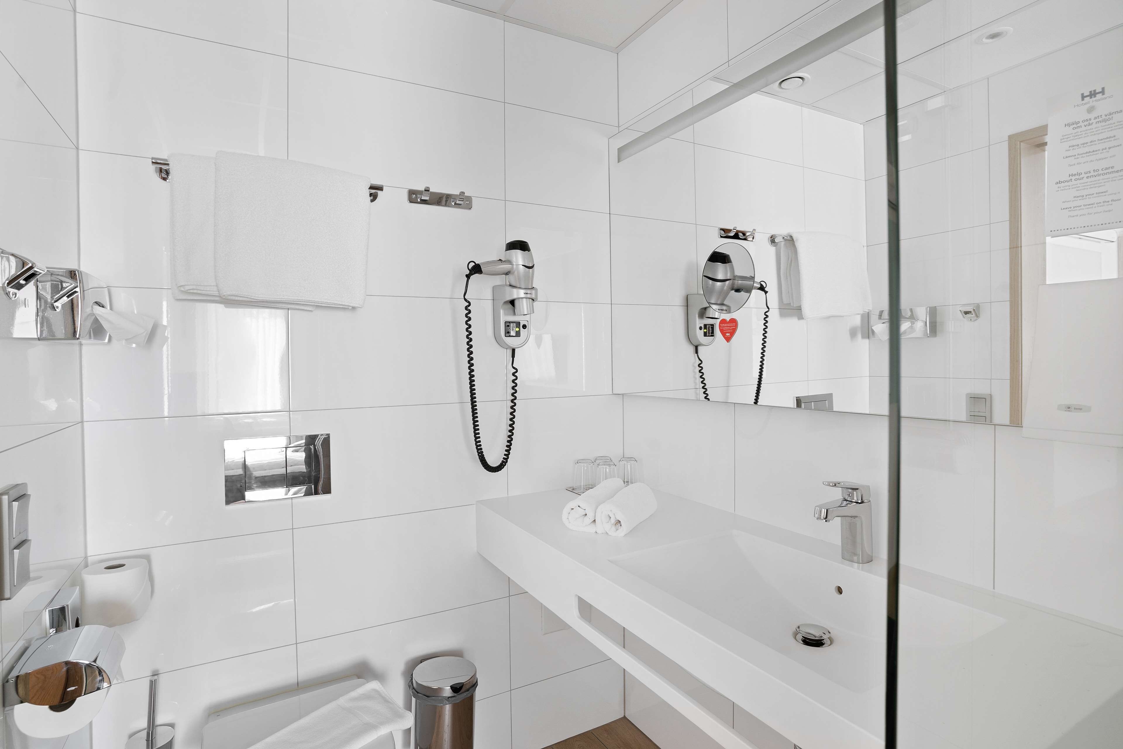 Un baño moderno con azulejos blancos, cabina de ducha de vidrio, tocador con lavamanos y espejo.