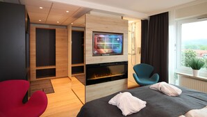 A modern hotel room with a large bed, a TV mounted on the wall, a seating area with a red chair, and a view of the outdoors through a window. - Best Western Hotel Halland (Kungsbacka)