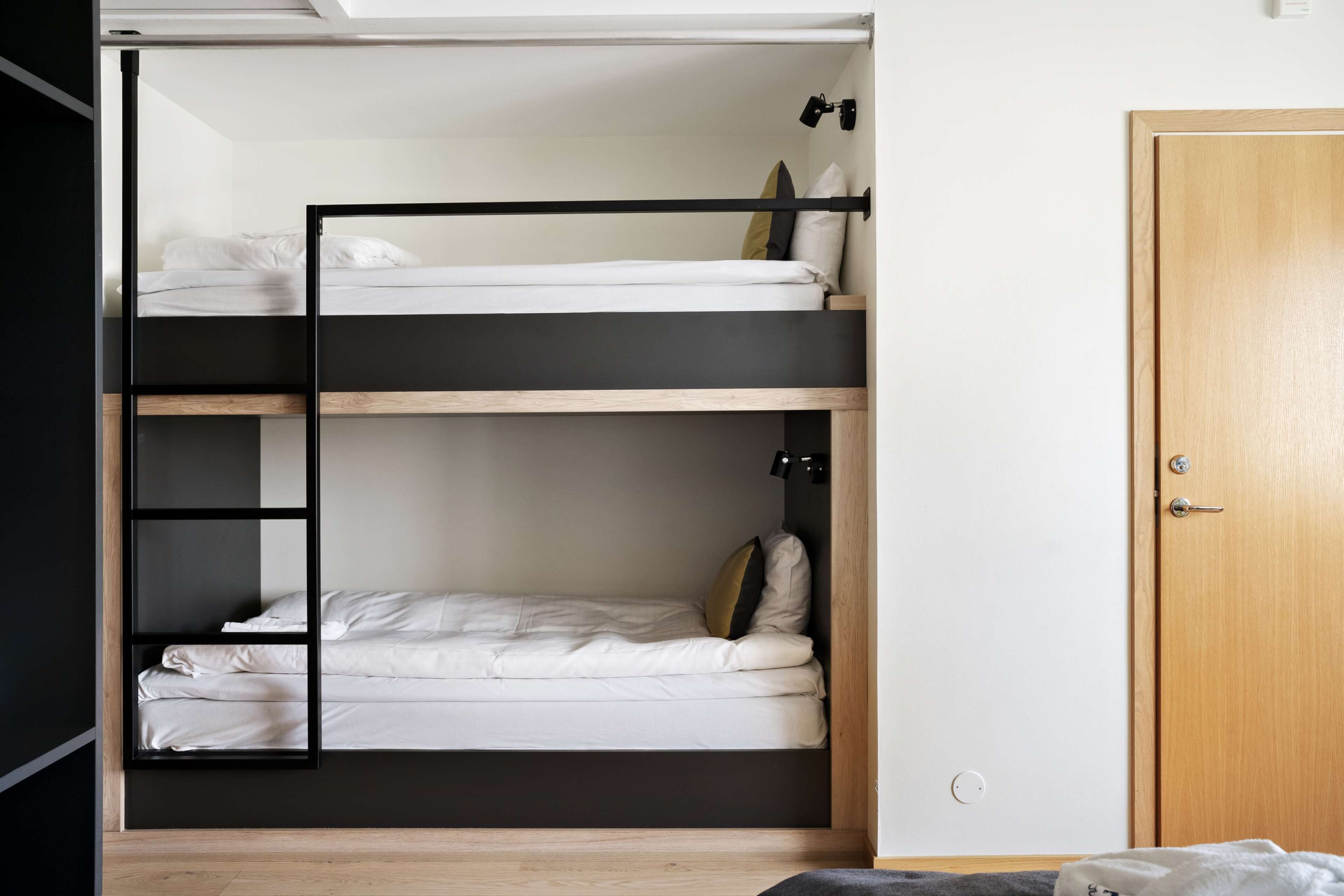 A bunk bed room with a wooden door and a light switch on the wall.
