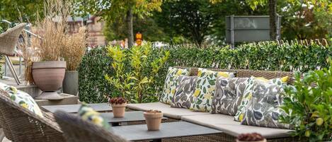 An outdoor seating area with wicker furniture, planters, and a hedge.