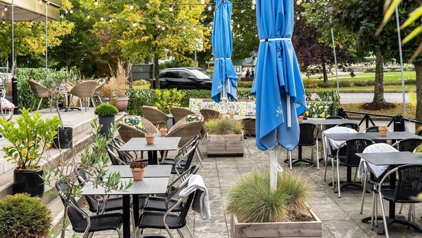 An outdoor patio with tables and chairs, some covered by blue umbrellas, and potted plants. - Best Western Hotel Halland (Kungsbacka)