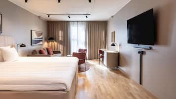 A hotel room with a bed, a desk, a chair, a TV, and a window with curtains.