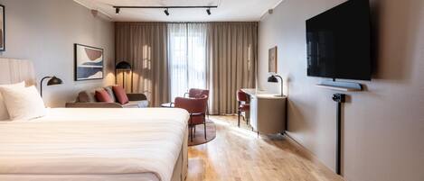 Habitación de hotel con cama, escritorio, silla, televisión y ventana con cortinas.