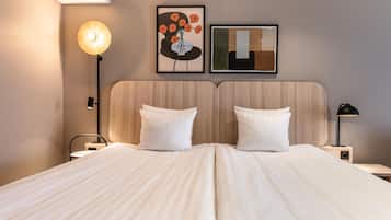 A double bed with a wooden headboard, two bedside tables, a floor lamp, and two framed artworks on the wall.