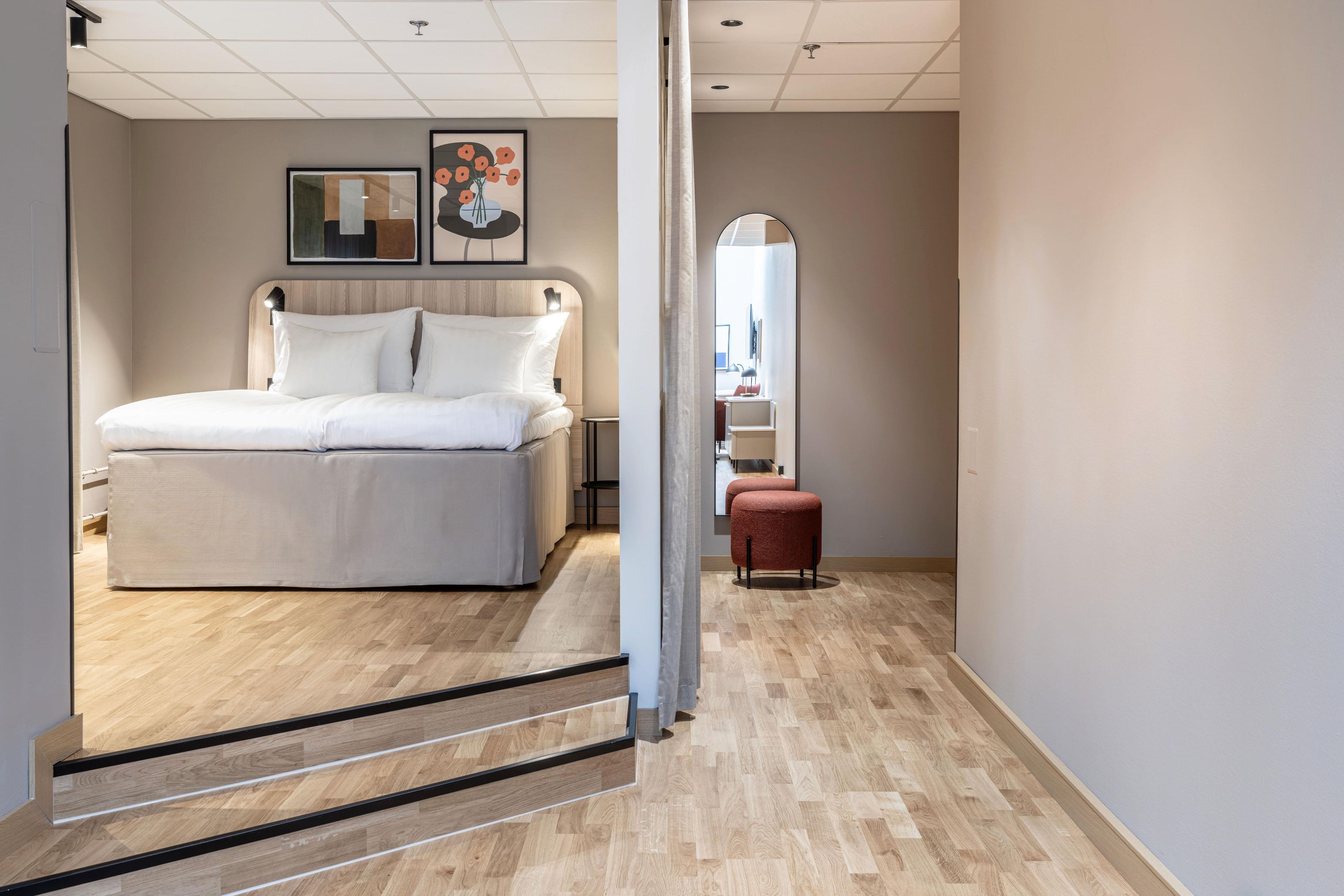 A modern hotel room with a large bed, a small seating area, and a mirror on the wall.