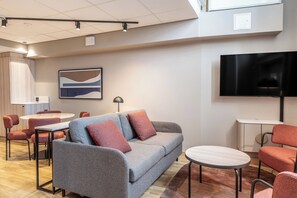 A modern hotel room with a grey sofa, red chairs, a round table, a flat-screen TV, and a painting on the wall. - Scandic Grand Marina (Helsinki)