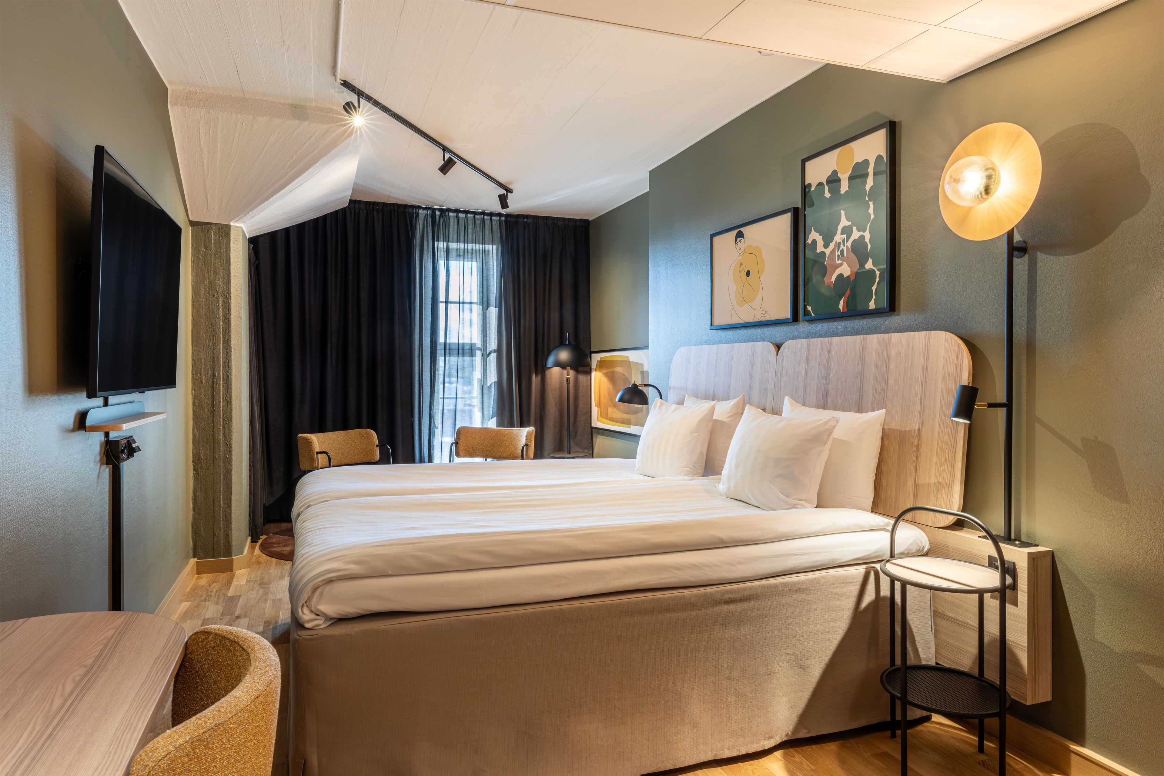 A hotel room with a large bed, a desk, a chair, and a TV.