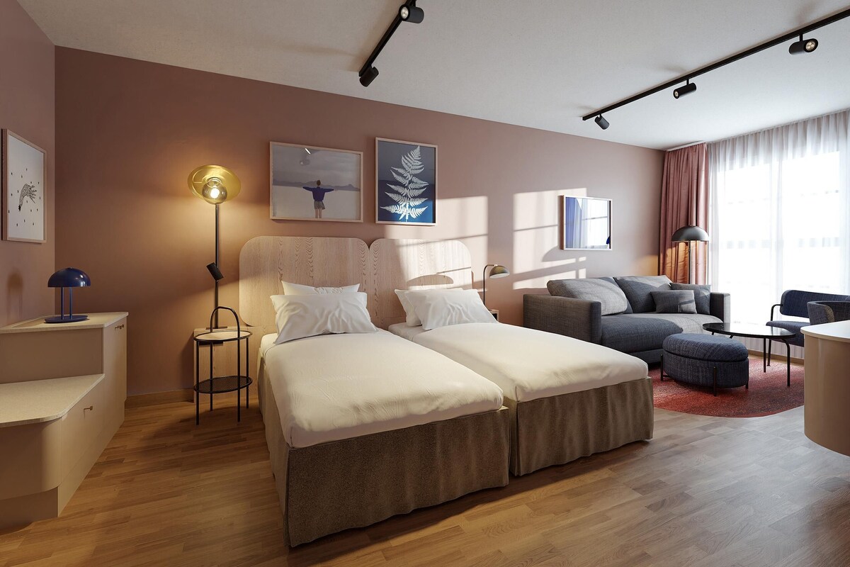 A modern hotel room with a bed, sofa, and desk area.