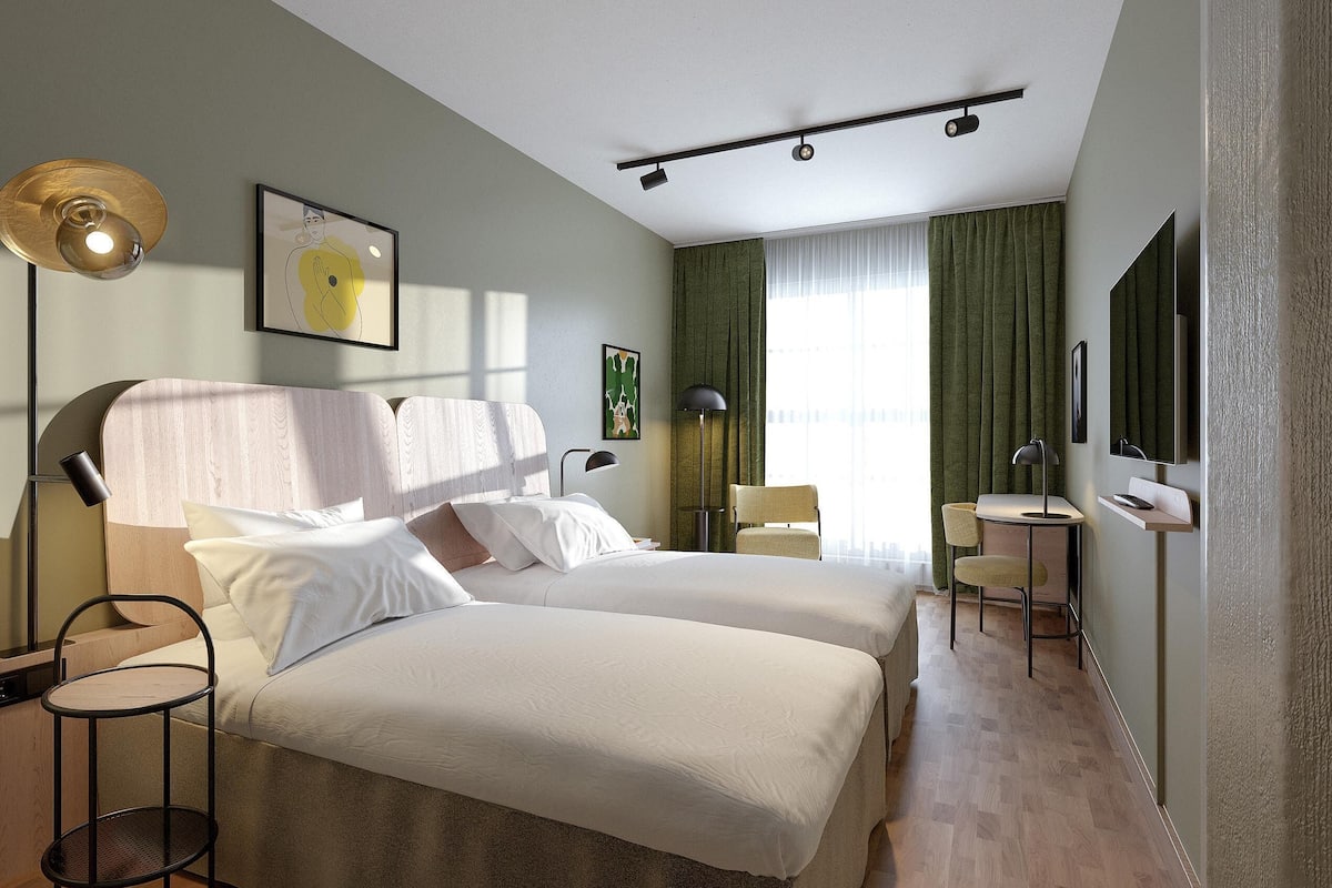Une chambre d’hôtel avec deux lits, un bureau, une chaise, un lampadaire et des œuvres d’art accrochées aux murs.