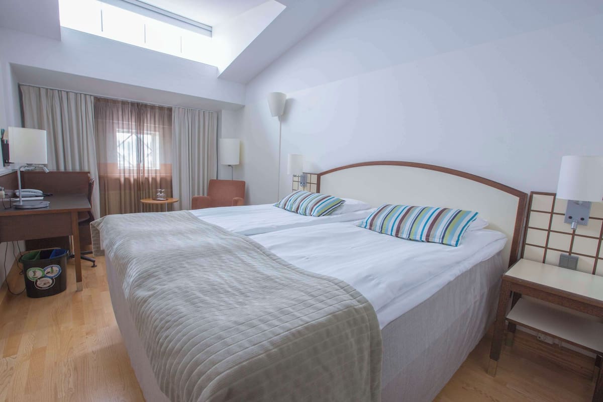 Une chambre d’hôtel avec un grand lit, un bureau, une chaise et une poubelle.