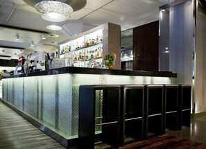 A modern bar area with a glass partition, shelves with bottles, and a seating area with black stools.