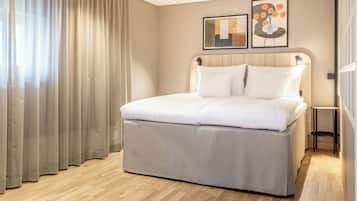 A hotel room with a bed, curtains, a small table, and two framed pictures on the wall.