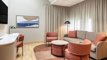 A modern living room with a sofa, chairs, a coffee table, a flat-screen TV, and a painting on the wall.