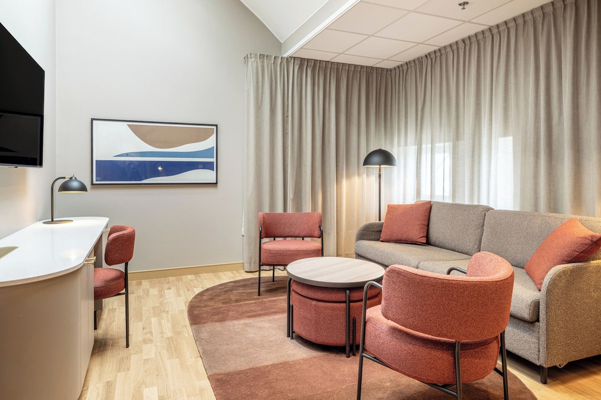 Un salon moderne avec un canapé, des fauteuils, une table basse, un téléviseur et un tableau accroché au mur.