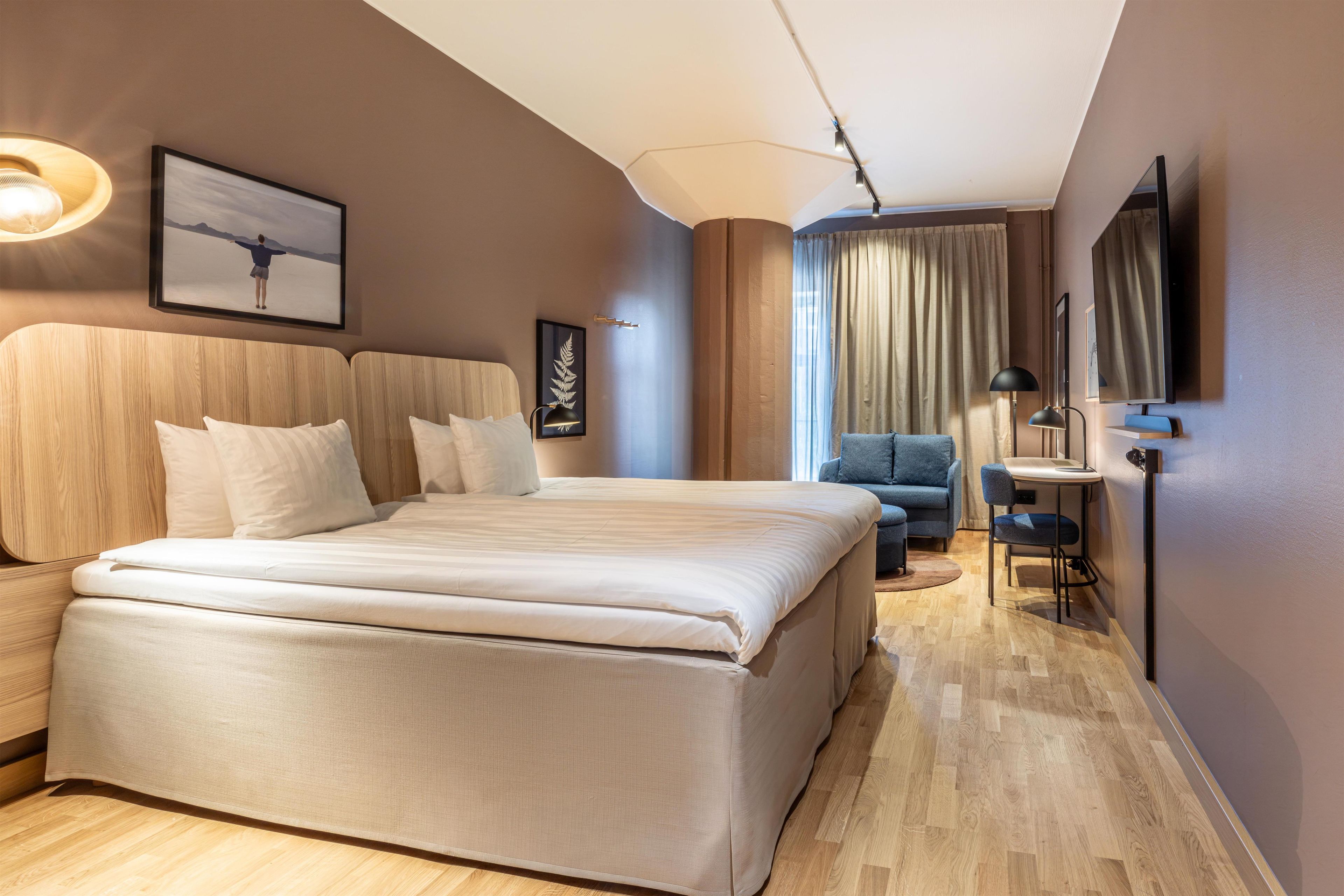 Ein modernes Hotelzimmer mit einem großen Bett, einem Schreibtisch, einem Sessel und einem Fernseher.