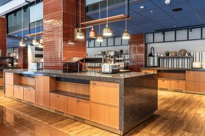 A modern kitchen with a central island, wooden cabinets, and a backsplash with a repeating pattern. - Scandic Grand Marina (Helsinki)