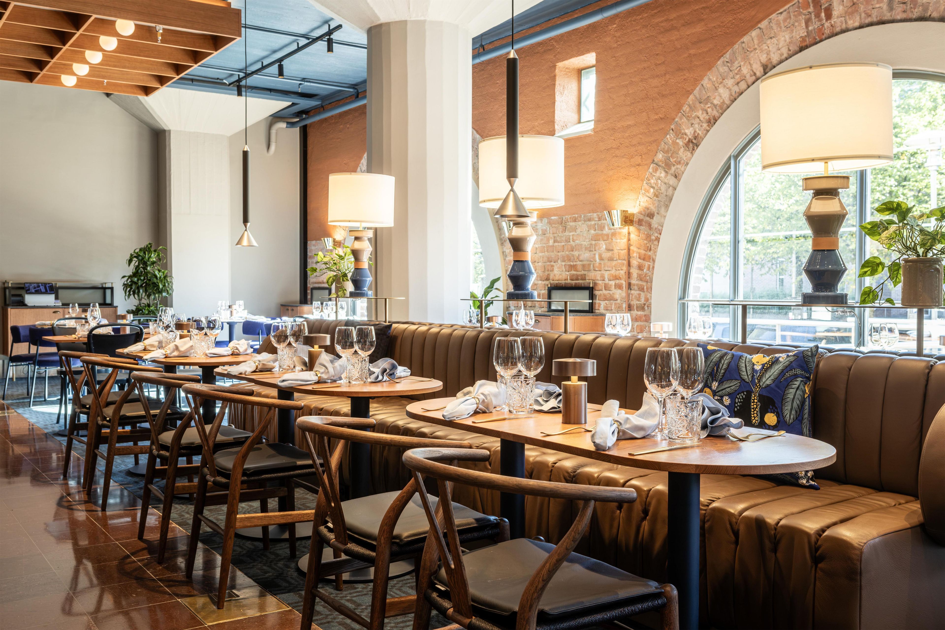 Een restaurantinterieur met leren banken, houten tafels en hangende pendelverlichting.