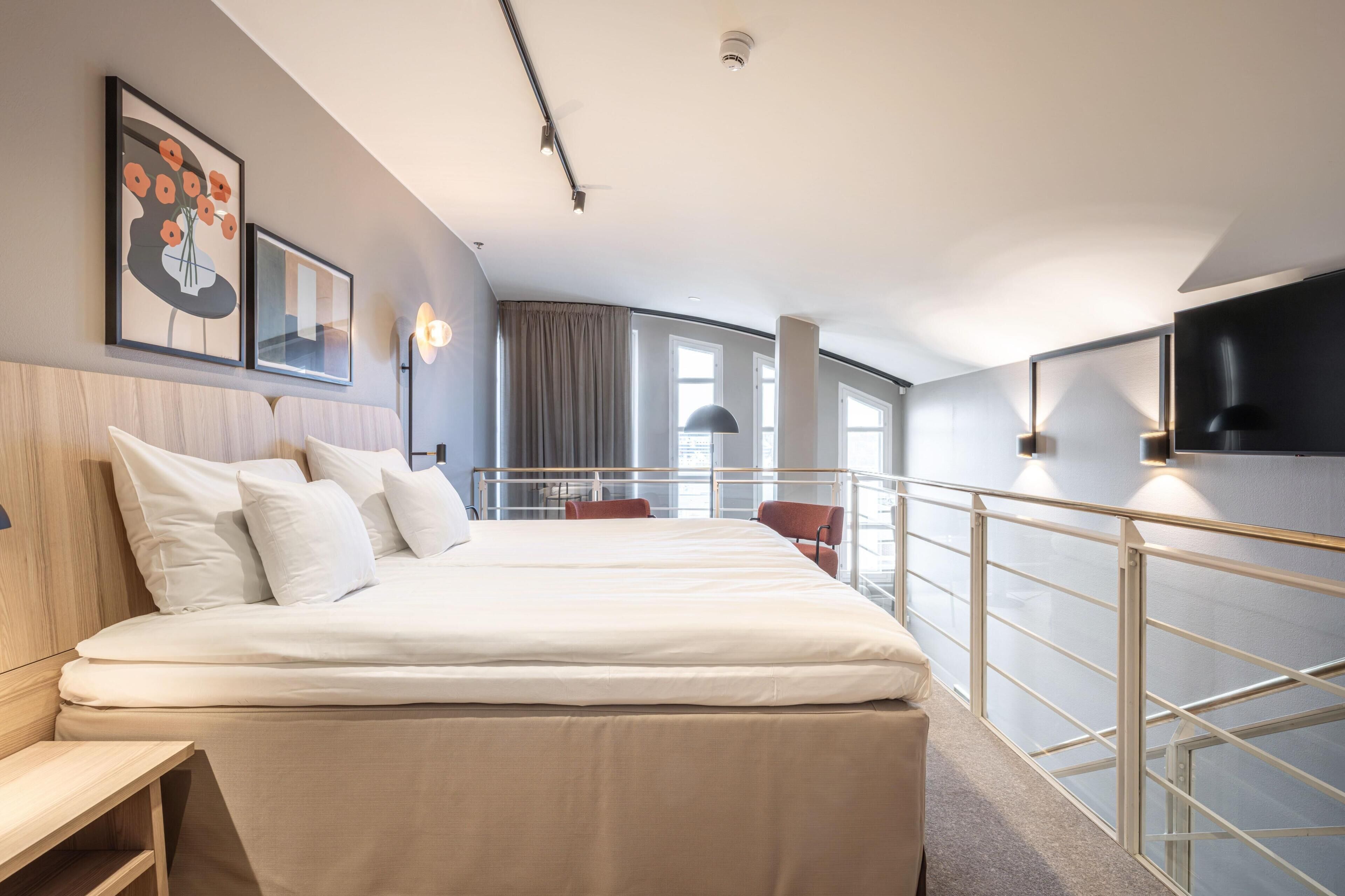 A hotel room with a bed, bedside tables, a TV, a balcony with a railing, and a window.
