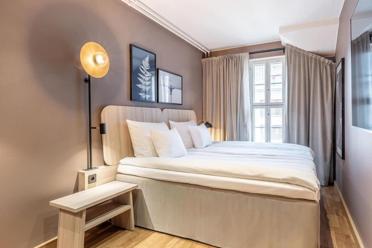 Une chambre à coucher avec un lit, une table de chevet, une lampe et des rideaux.