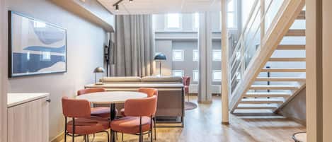 Un interior moderno con comedor, sofá, escalera y un amplio ventanal.
