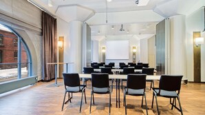 A conference room with a long table, chairs, a projector screen, and a large window with curtains. - Scandic Grand Marina (Helsinki)