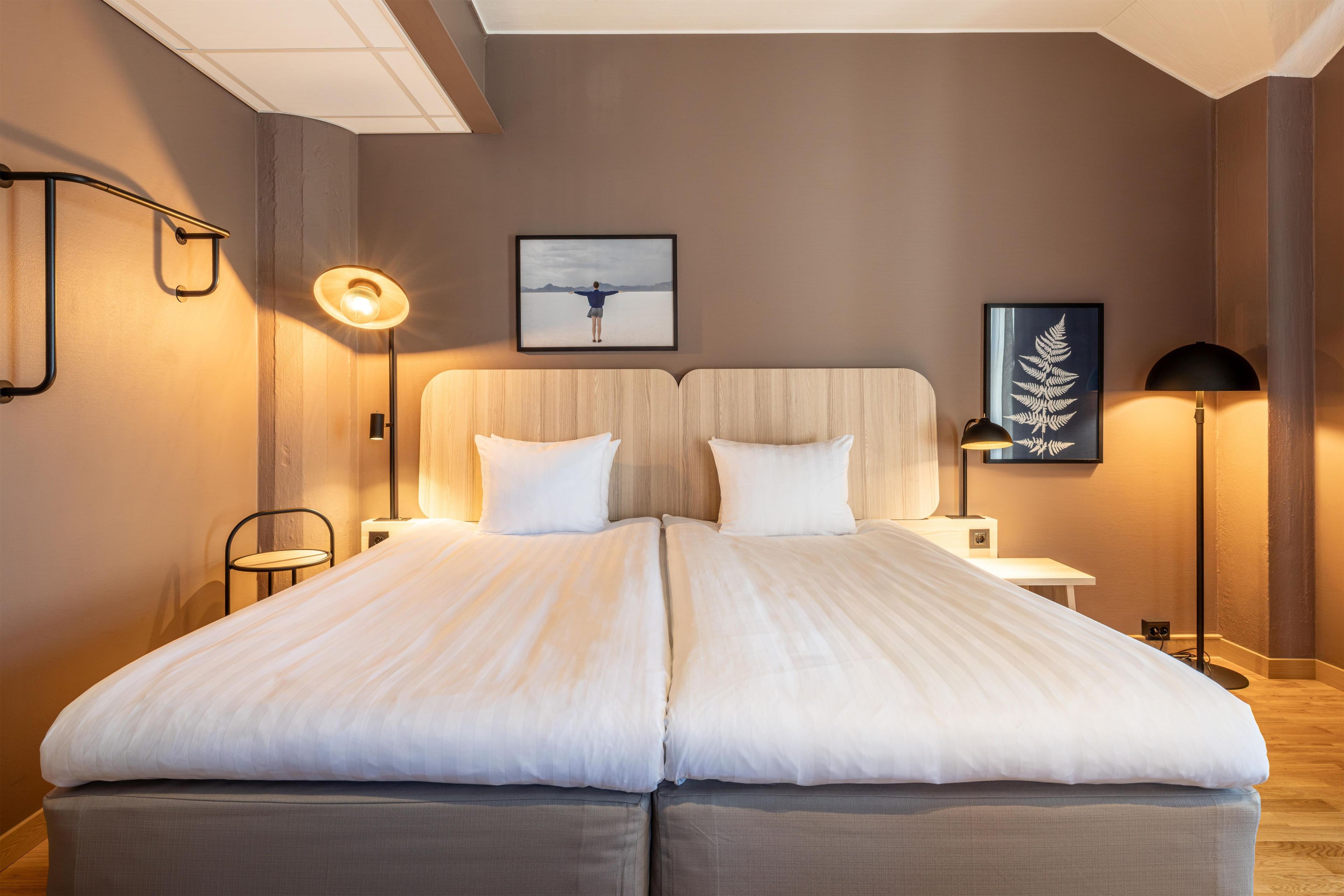 A double bed with a wooden headboard, two bedside tables, a framed picture on the wall, and a floor lamp.