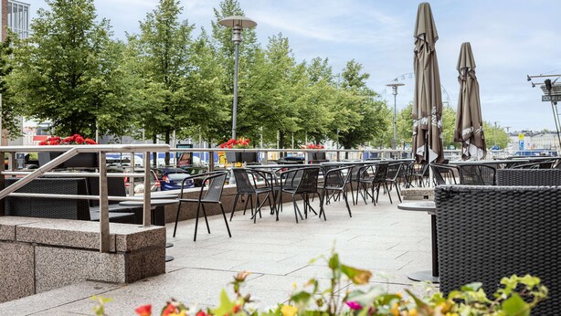 An outdoor seating area with tables and chairs, a lamp post, and umbrellas. - Scandic Grand Marina (Helsinki)