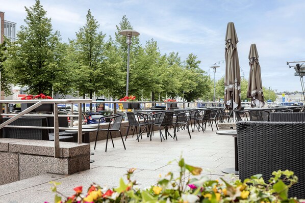 An outdoor seating area with tables and chairs, a lamp post, and umbrellas. - Scandic Grand Marina (Helsinki)