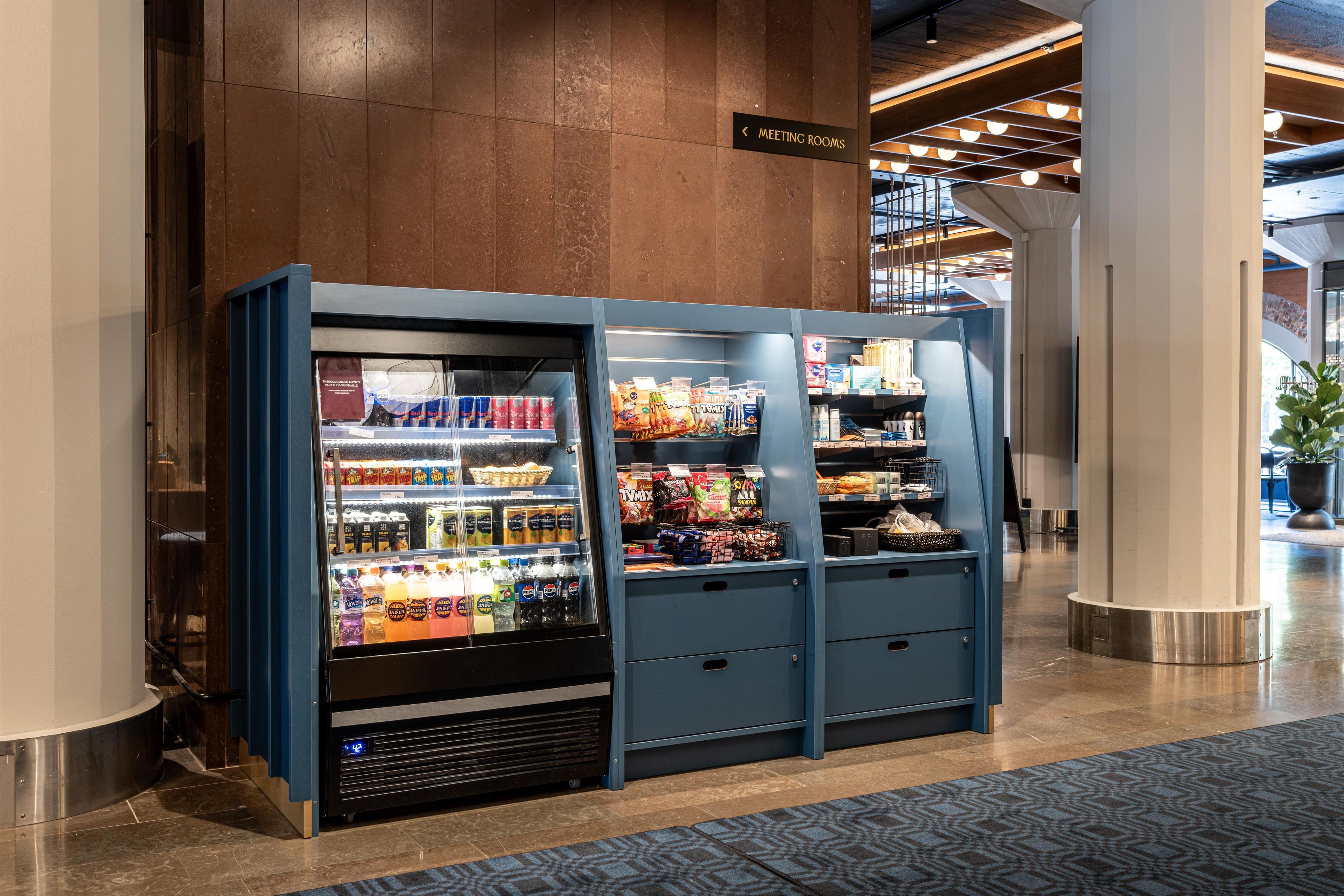 A vending machine with beverages and snacks, located in a lobby with a sign for meeting rooms.