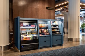 A vending machine with beverages and snacks, located in a lobby with a sign for meeting rooms.