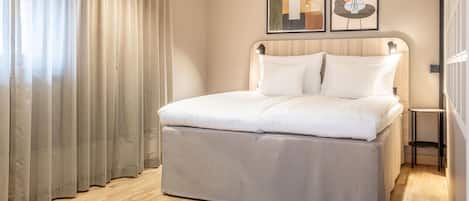 Una habitación de hotel moderna con una cama grande, piso de madera y dos cuadros enmarcados en la pared.