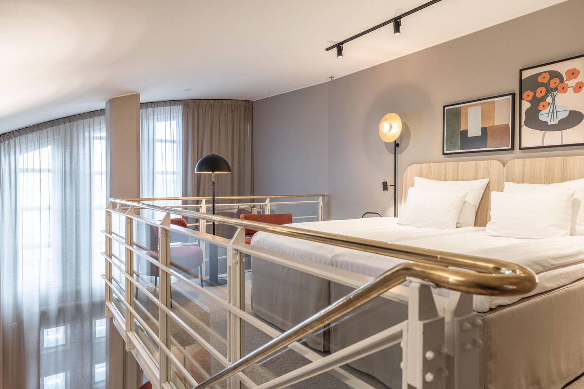 Une chambre d’hôtel moderne équipée d’un lit, d’un bureau, d’une chaise, d’une lampe et offrant une vue sur l’extérieur.
