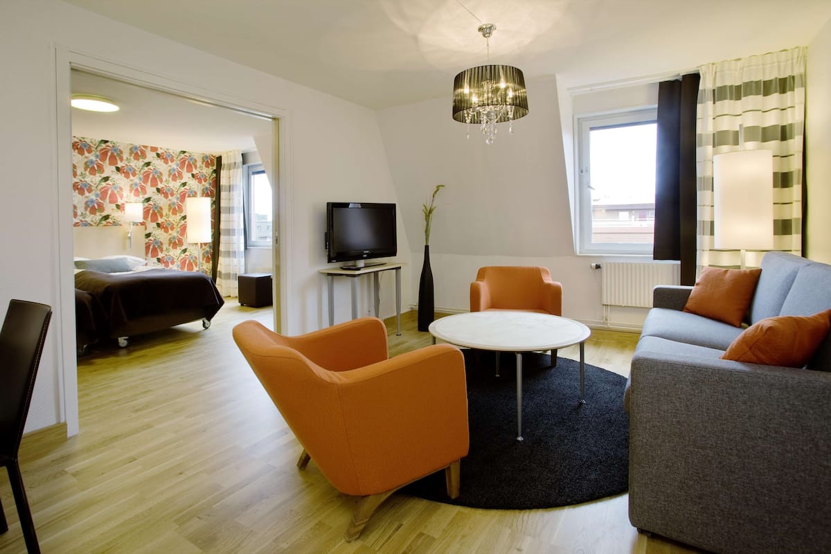 A modern living room with a sofa, armchairs, a TV, and a chandelier.