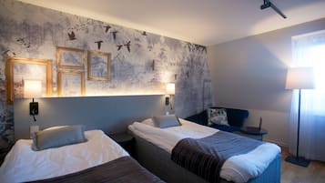 Ett hotellrum med två sängar, ett skrivbord, en lampa och en vägg med inramade tavlor.
