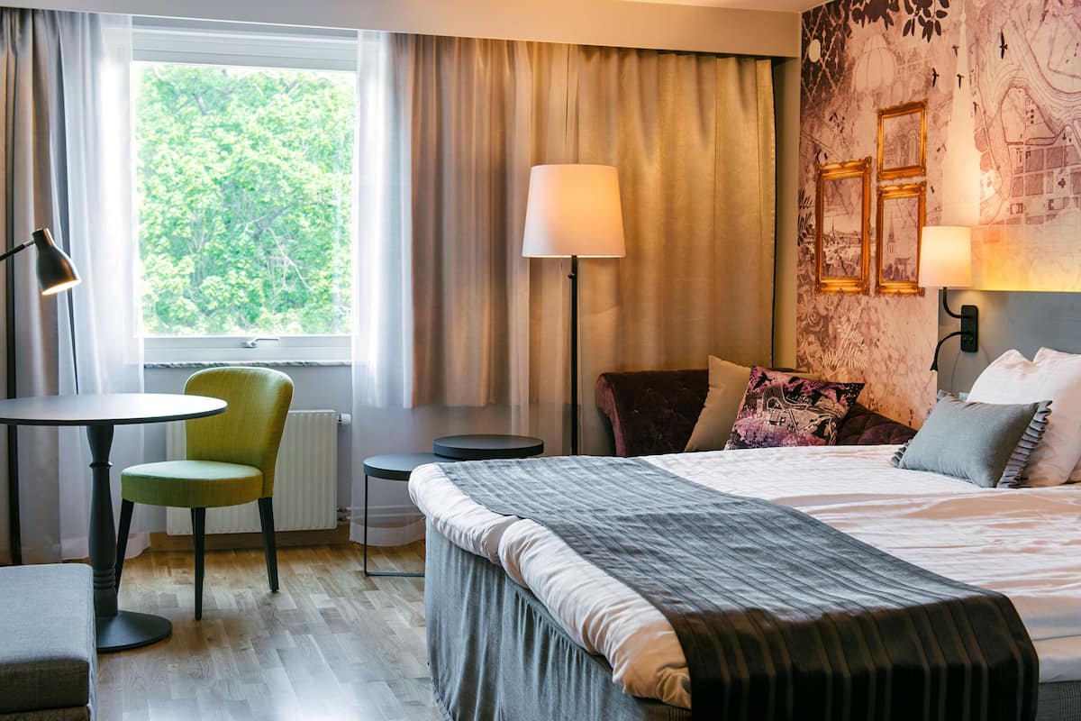 A hotel room with a bed, a chair, a table, and a lamp.