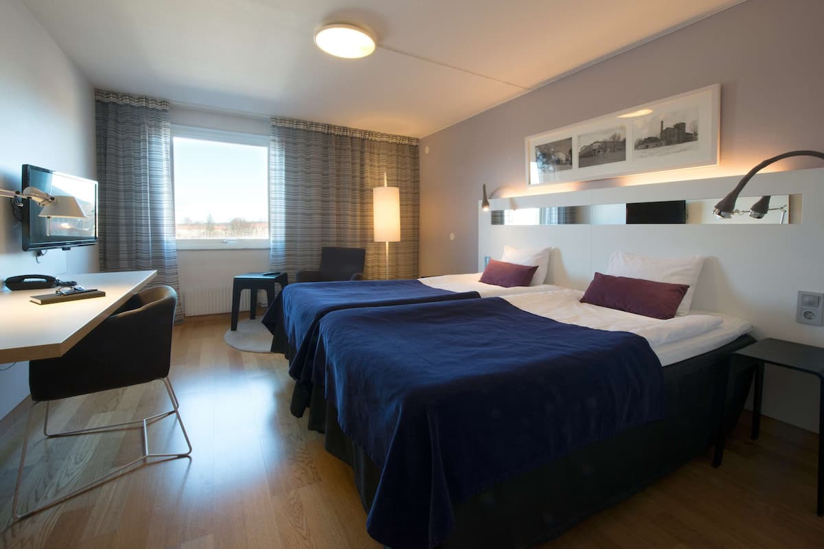 A hotel room with two beds, a desk, a chair, a TV, and a window with curtains.