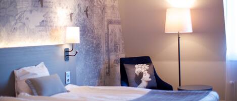A hotel room with a large bed, a nightstand, a lamp, and a wall with a mural.
