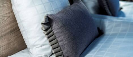 A bed with a patterned bedspread and multiple pillows, including a grey one with a ruffled edge.