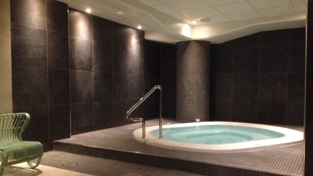 A spa area with a hot tub, a green chair, and dark tiled walls. - Scandic Winn (Karlstad)