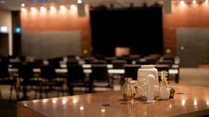 A conference room with a stage, rows of chairs, and a table with decorative items. - Scandic Winn (Karlstad)