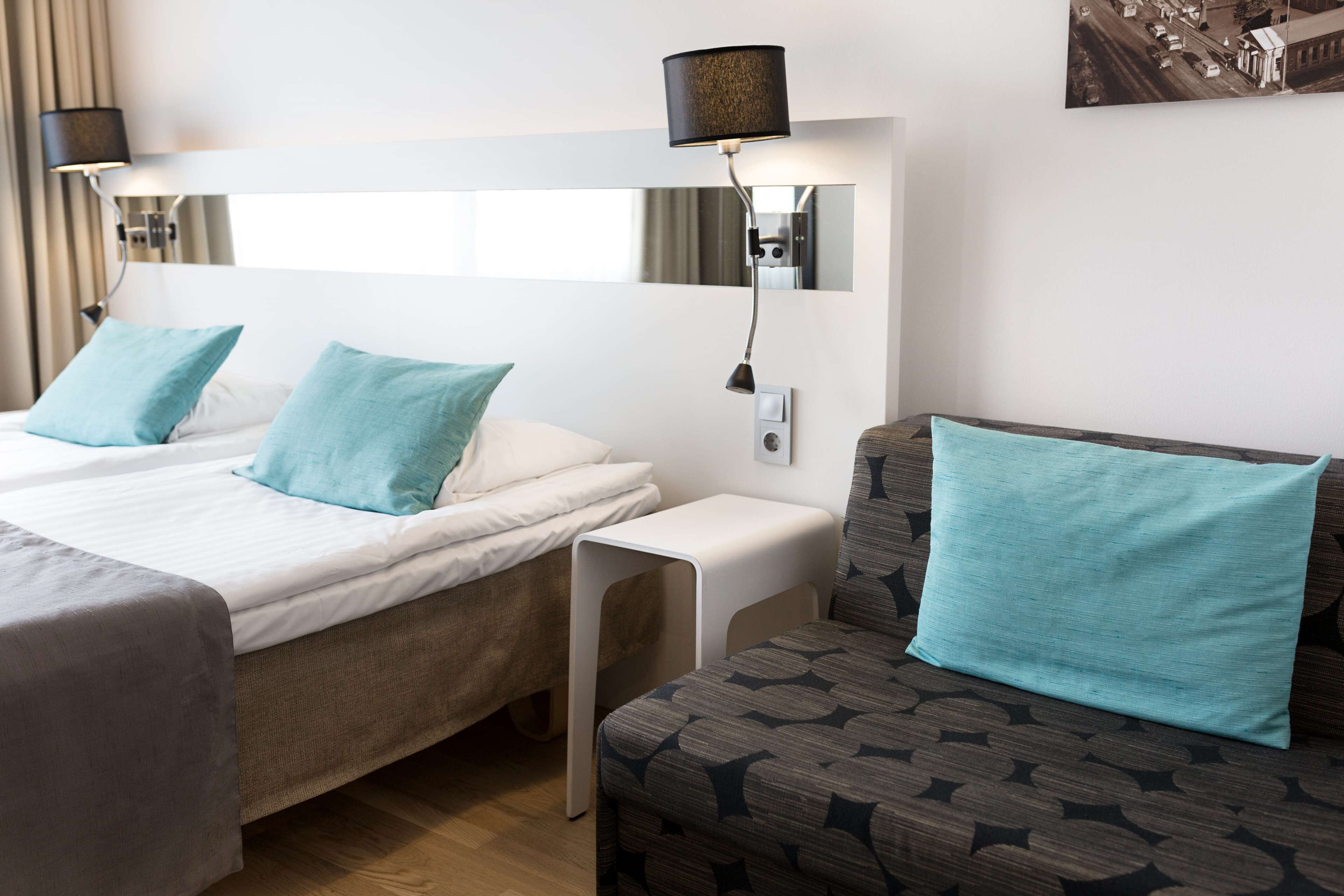 A hotel room with two beds, a sofa, a nightstand, and a wall-mounted lamp.