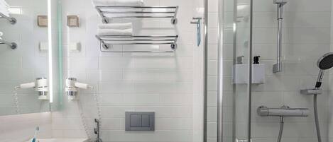 A modern bathroom with a glass shower enclosure, a towel rack, a toilet paper holder, and a hairdryer.